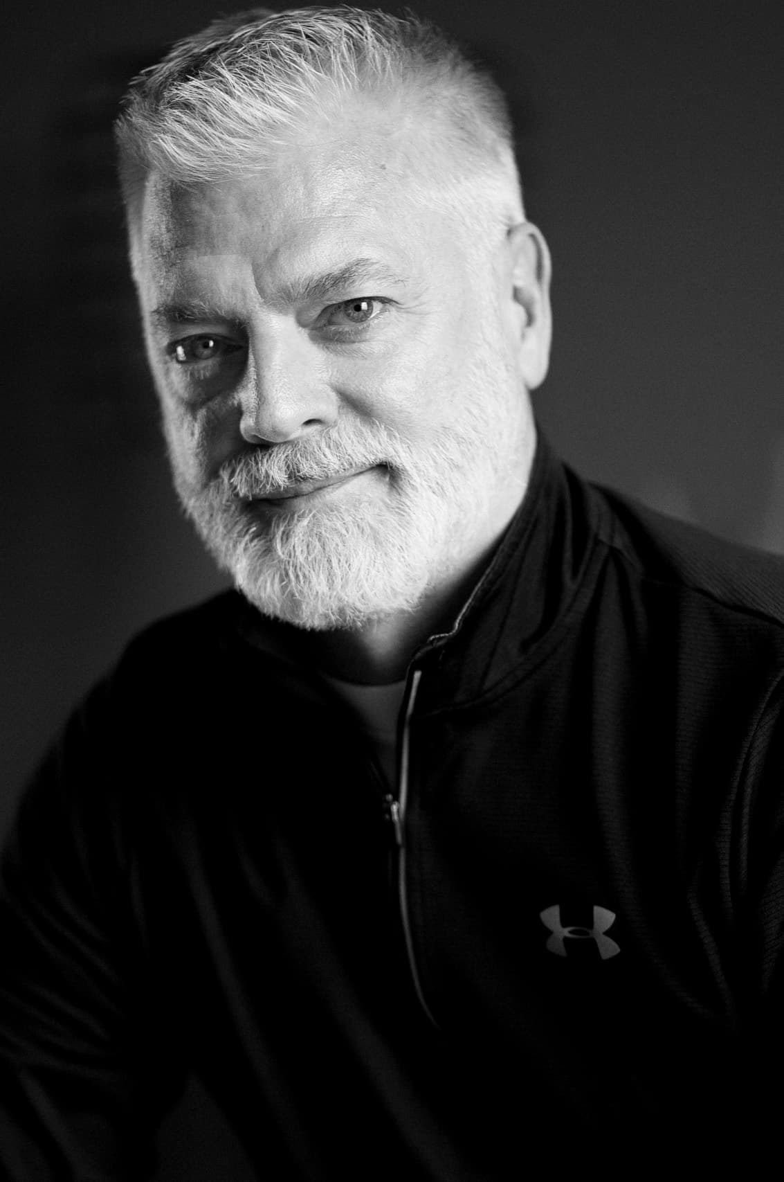 Black and white business portrait of a grey bearded man in a black sweatshirt